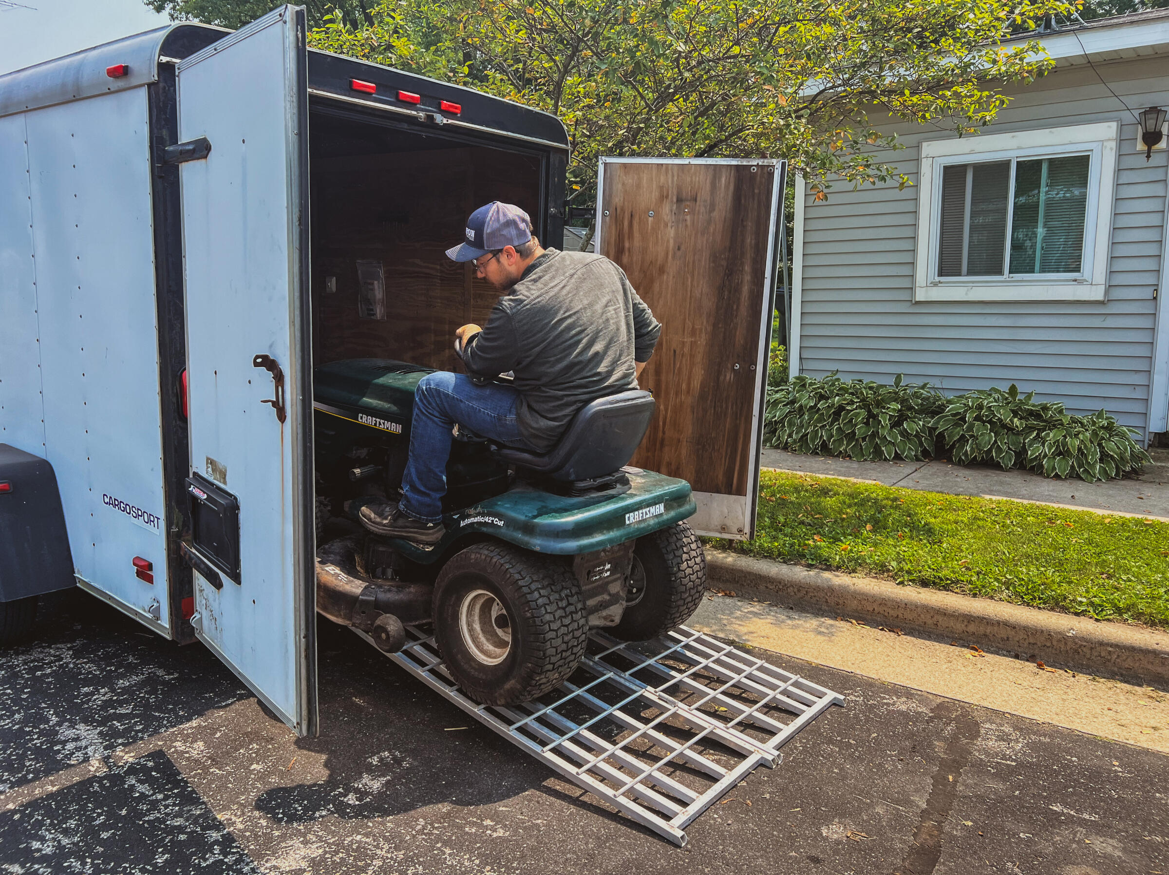 Small engine repair pickup service – mechanic loading a Craftsman riding lawn mower into a trailer for transport in Cambridge, Wisconsin.